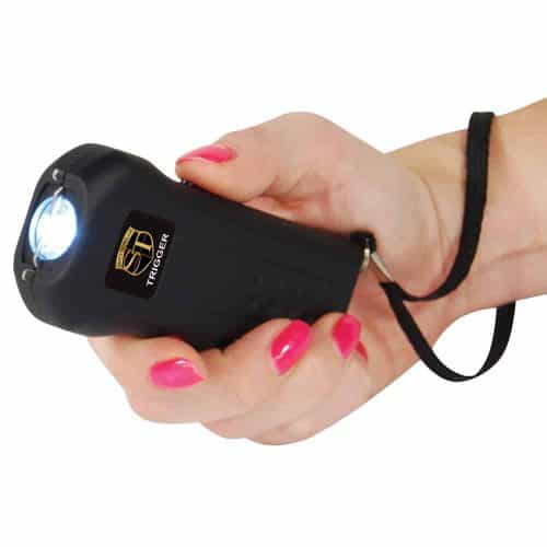 Hand holding black stun gun with a strap, discharging light, for personal security and defense.