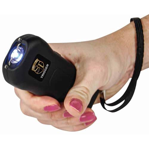 Close-up of a hand holding a black stun gun with a glowing tip and wrist strap for self-defense.
