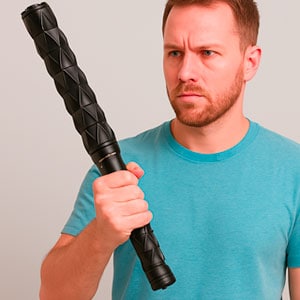 Man in teal shirt holds a textured black baton, appearing focused, against a neutral background.